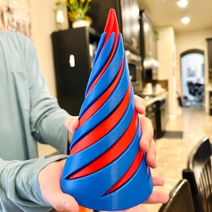 May include: A blue and red spiral-shaped decorative object. The object is held by a person and has a conical shape with alternating blue and red bands. The top of the object is red.