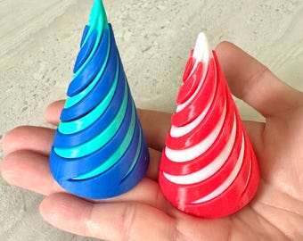 May include: Two cone-shaped decorative objects. One is blue with turquoise stripes, the other is red with white stripes. The objects are held in a hand, showcasing their spiral design and vibrant colors. They appear to be made of plastic.