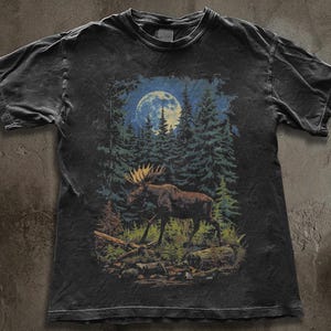 May include: Black t-shirt with a forest scene featuring a moose under a full moon. The graphic includes pine trees and a moose with antlers. The shirt has a vintage, worn appearance, with a faded look.