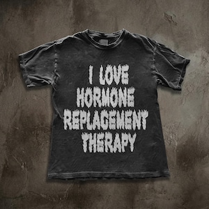 Puede incluir: Una camiseta gris oscuro con el texto blanco "I LOVE HORMONE REPLACEMENT THERAPY" en letras desgastadas. La camiseta tiene un aspecto vintage y desgastado.
