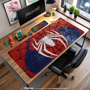 Peut inclure: Tapis de bureau avec un motif Spider-Man. Le tapis présente un motif de toile d'araignée rouge avec un emblème d'araignée blanc sur un fond bleu et rouge. Le tapis mesure 60cm x 120cm. La marque "Pixavaa" est visible.