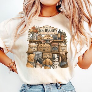 A woman wearing a white t-shirt with a graphic design of dogs and a bakery.