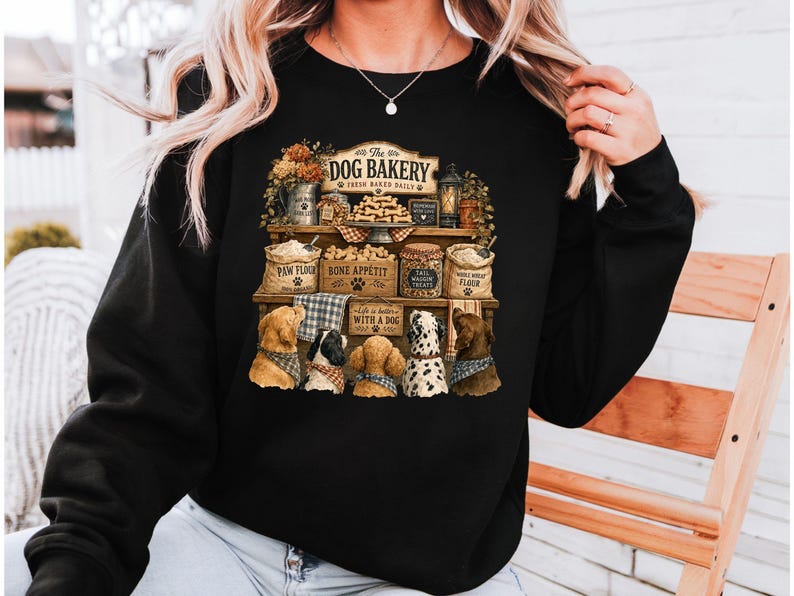 A woman wearing a black sweater with a graphic design depicting a dog bakery with various dog-related items and illustrations.