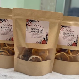 Peut inclure: Trois sachets en papier kraft de pot-pourri de Noël. Chaque sac a une fenêtre transparente montrant des tranches d'orange séchées, de l'anis étoilé et d'autres épices. Les sacs ont une étiquette avec des instructions.