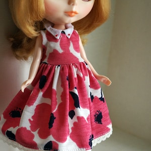 May include: A doll with blonde hair wearing a red and white floral dress with a white collar and red shoes.