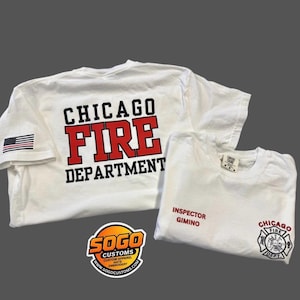 May include: Two white t-shirts with Chicago Fire Department graphics. One shirt features the text "CHICAGO FIRE DEPARTMENT" in red and black, with an American flag on the sleeve. The other shirt has "INSPECTOR GIMINO" and a Chicago Fire Dept. logo.