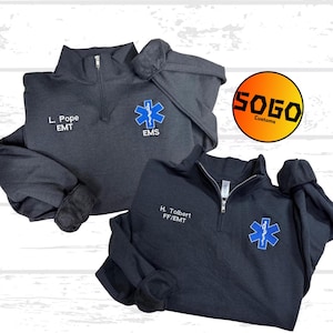 Puede incluir: Dos jerséis grises oscuros y negros con cremallera de cuarto. Uno tiene "L. Pope EMT" y un símbolo de EMS. El otro tiene "H. Tolbert FF/EMT" y un símbolo de EMS. Los jerséis tienen cierre de cremallera y un pequeño logotipo bordado.