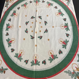 May include: A white Christmas tablecloth with a green and red border. The tablecloth features a circular design with candles, holly, and star accents. The design is repeated around the border and across the surface.
