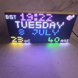 Może przedstawiać: Cyfrowy zegar wyświetlający godzinę 19:22, wtorek, lipiec, 23&deg;C i 40 AQI. Zegar ma czarną tarczę z białymi, niebieskimi, zielonymi i ż&oacute;łtymi diodami LED. G&oacute;ra i boki są ż&oacute;łte.