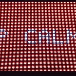 Może przedstawiać: Zbliżenie czerwonego wyświetlacza LED z napisem "KEEP CALM" w białych, pikselowanych literach. Tło to siatka małych, podświetlonych czerwonych kropek. Całość ma retro, cyfrowy wygląd.