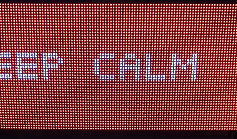 Może przedstawiać: Zbliżenie czerwonego wyświetlacza LED z napisem "KEEP CALM" w białych, pikselowanych literach. Tło to siatka małych, podświetlonych czerwonych kropek. Całość ma retro, cyfrowy wygląd.