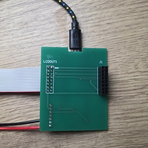 Może przedstawiać: Zielona płytka drukowana z nadrukiem "LCDOUT1" i "J1". Czarny kabel USB jest podłączony do płytki. Podłączona jest r&oacute;wnież taśma i czerwone i czarne przewody.
