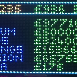 Może przedstawiać: Cyfrowy wyświetlacz pokazuje dane finansowe w zielonym i niebieskim tekście matrycy punktowej. Wyświetlacz pokazuje kategorie takie jak ISA, Bonds i Pension, z odpowiadającymi im wartościami pieniężnymi. G&oacute;rny wiersz wyświetla wartość &pound;261236.