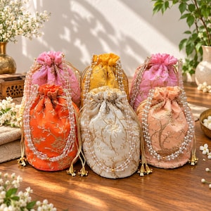 May include: A collection of six drawstring pouches in pink, yellow, orange, white, and peach colors. Each pouch features intricate gold floral embroidery and a decorative handle made of multiple strands of small white faux pearls with gold tassels.