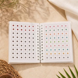 May include: A spiral-bound notebook featuring pages filled with rows of small, circular adhesive stickers. The left page displays red and black-and-white checkered patterns, while the right page showcases a variety of colorful, solid-toned stickers.