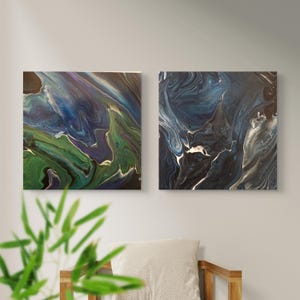 May include: Two square canvas wall art pieces featuring abstract fluid acrylic paint designs. The left panel displays swirling shades of deep green, blue, and purple. The right panel showcases a dark composition of navy, black, and white marble-like patterns.