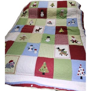 May include: A patchwork Christmas quilt featuring squares of red, green, blue, and white. Each square has an embroidered holiday design, including snowmen, reindeer, Christmas trees, and Santa Claus. The quilt has a white backing and a red and blue border.