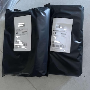 May include: Two black poly mailer shipping packages with white address labels. The packages are sealed and ready for shipment. The labels have barcodes and text.