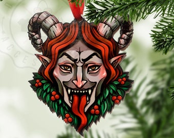 May include: A wooden Christmas ornament shaped like a demon's head with red horns, red hair, and a green holly wreath around the neck. The demon has a menacing expression with a large, red tongue sticking out.