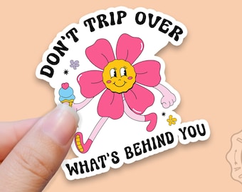 May include: A pink flower with a smiling face and arms and legs is running with an ice cream cone. The text "Don't trip over what's behind you" is written around the flower.