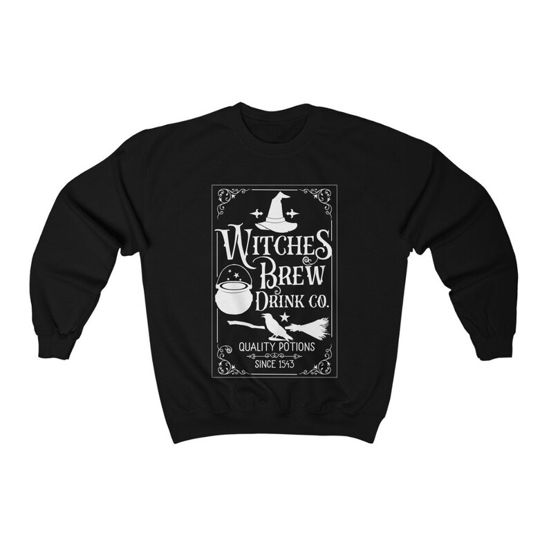 May include: Black sweatshirt with a white graphic featuring a witch's hat, cauldron, broom, and the text "Witches Brew Drink Co. Quality Potions Since 1543". The design is centered on the front of the long-sleeved top.