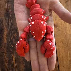 May include: A bright red lobster figurine with white polka dots. The lobster is held in a hand, showcasing its detailed design. The figurine's claws and body segments are clearly defined, creating a realistic appearance. The lobster is a decorative item.