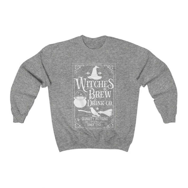 May include: A heather gray sweatshirt featuring a white graphic that reads "Witches Brew Drink Co." with a witch's hat, cauldron, and broom. The text "Quality Potions Since 1543" is also included in the design. The sweatshirt has long sleeves and a crew neck.