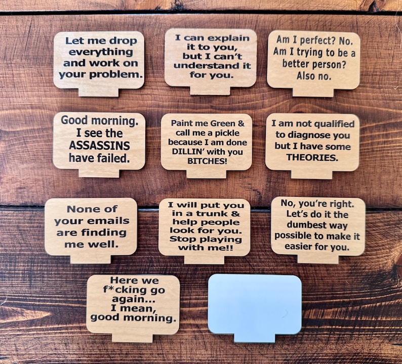 May include: A collection of wooden desktop-shaped signs with humorous phrases in black text. The signs include phrases like "Let me drop everything and work on your problem" and "I am not qualified to diagnose you but I have some THEORIES."
