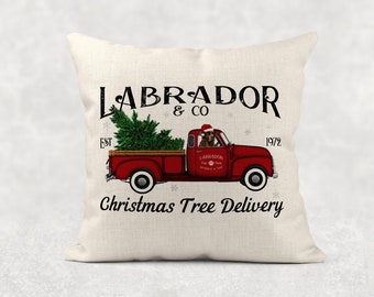 May include: A red pickup truck with a Christmas tree in the back and a Labrador Retriever wearing a Santa hat in the driver's seat. The truck has the text "LABRADOR & CO" and "Christmas Tree Delivery" on it.
