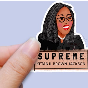 Pu&ograve; includere: Un adesivo con un'illustrazione a cartone animato di Ketanji Brown Jackson, la prima donna nera a servire nella Corte Suprema degli Stati Uniti. L'adesivo ha uno sfondo marrone con il testo "SUPREME" e "KETANJI BROWN JACKSON" in nero.