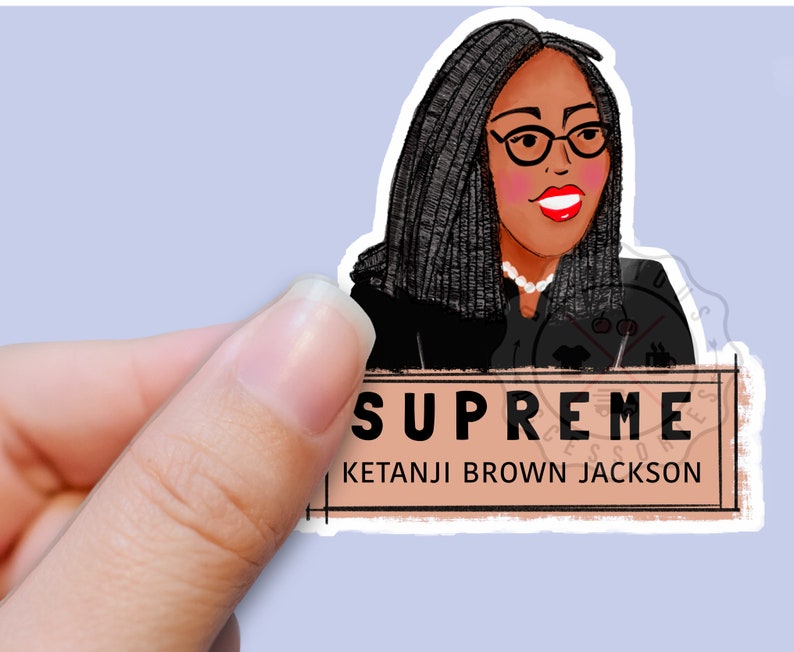 Pu&ograve; includere: Un adesivo con un'illustrazione a cartone animato di Ketanji Brown Jackson, la prima donna nera a servire nella Corte Suprema degli Stati Uniti. L'adesivo ha uno sfondo marrone con il testo "SUPREME" e "KETANJI BROWN JACKSON" in nero.