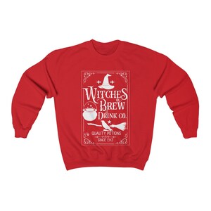 May include: A red sweatshirt featuring a white graphic with the text "Witches Brew Drink Co." and illustrations of a witch's hat, cauldron, bird, and broom. The text "Quality Potions Since 1543" is also included.