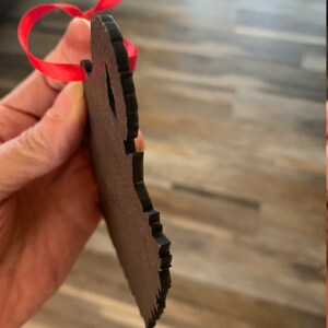 May include: A wooden ornament shaped like a bear with a red ribbon attached. The ornament is brown and has a rough texture.