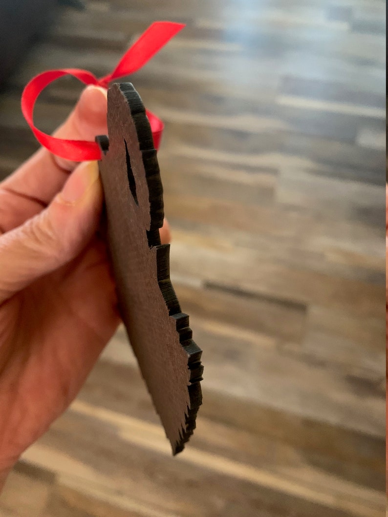 May include: A wooden ornament shaped like a bear with a red ribbon attached. The ornament is brown and has a rough texture.