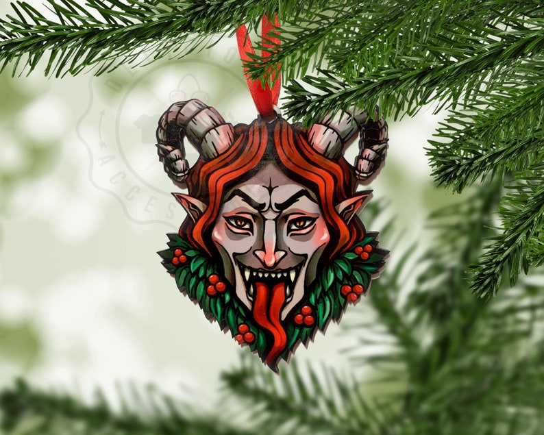 May include: A wooden Christmas ornament shaped like a demon's head with red horns, red hair, and a green holly wreath around the neck. The demon has a menacing expression with a large, red tongue sticking out.