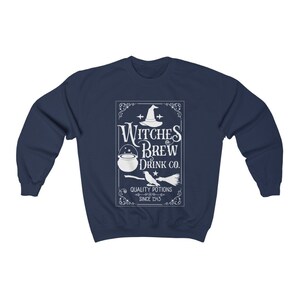 May include: Navy blue sweatshirt with a white graphic that reads "Witches Brew Drink Co." The design includes a witch's hat, cauldron, broom, and the text "Quality Potions Since 1543". A cozy, long-sleeved top for Halloween or everyday wear.