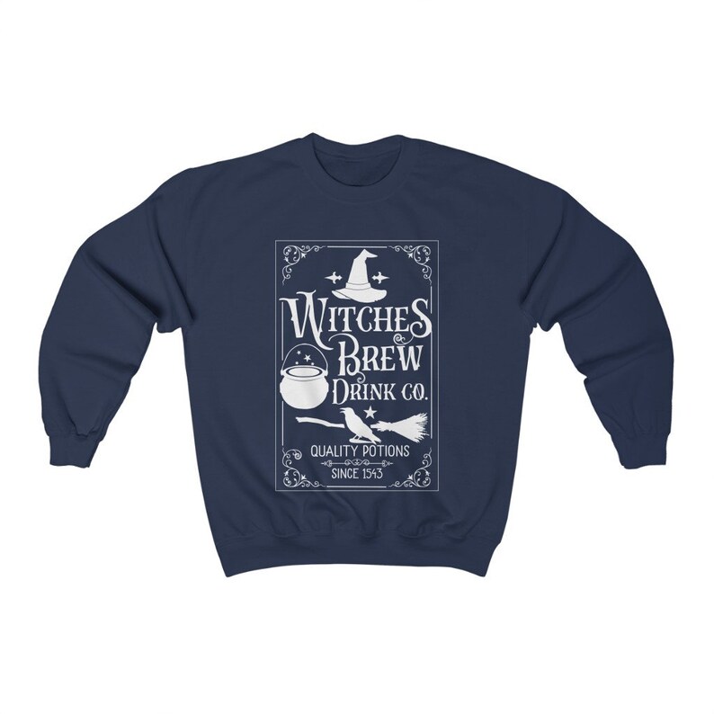 May include: Navy blue sweatshirt with a white graphic that reads "Witches Brew Drink Co." The design includes a witch's hat, cauldron, broom, and the text "Quality Potions Since 1543". A cozy, long-sleeved top for Halloween or everyday wear.