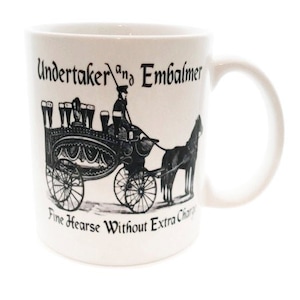 May include: White ceramic mug with a black and white illustration of a horse-drawn hearse with the text "Undertaker and Embalmer Fine Hearse Without Extra Charge".