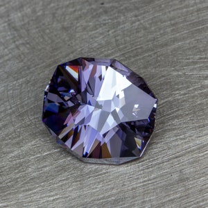 May include: A faceted purple gemstone with a clear center, set against a gray background.