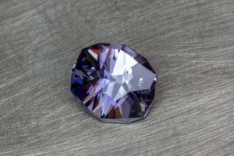 May include: A faceted purple gemstone with a clear center, set against a gray background.
