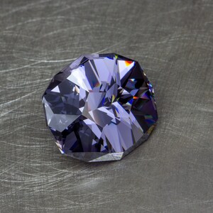 May include: A large, faceted, purple gemstone with a dark, almost black, hue. The gem is cut in a unique, octagonal shape and has a high degree of brilliance.