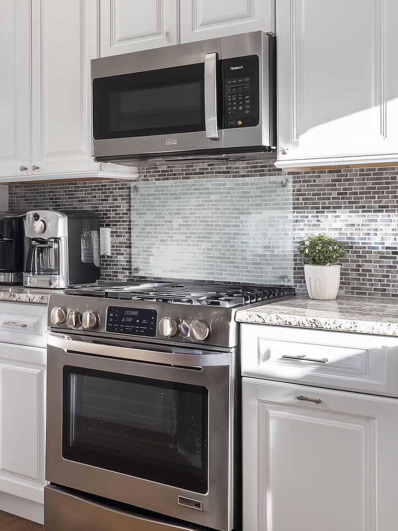 May include: A stainless steel gas range with a matching over-the-range microwave, positioned below white cabinets. The kitchen features a gray and white mosaic tile backsplash, a granite countertop, and a small potted green plant on the side.