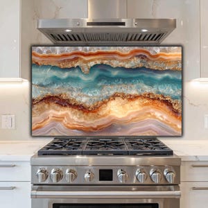 May include: A decorative kitchen backsplash featuring a layered agate design. The artwork showcases bands of blue, orange, and gold hues, creating a natural, abstract pattern. The backsplash is installed above a stainless steel stove and below a matching range hood.