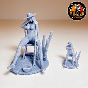 May include: A light blue miniature figurine of a woman in a cowboy hat, boots, and a seated pose, holding a rifle. The figurine is seated on a chair with a cactus and a small bowl. A smaller version of the figurine is also present.