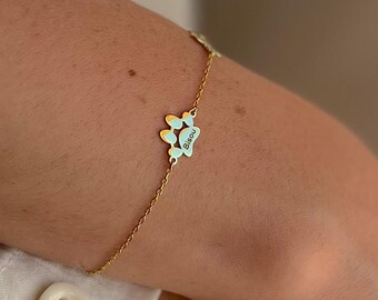 May include: A gold-colored chain bracelet featuring a paw print charm with a light blue enamel fill. The charm has the name "Bianca" engraved on it. The bracelet is worn on a person's wrist.