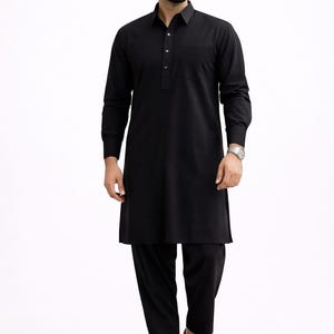May include: A black kurta pajama set. The long-sleeved kurta has a collared neckline and a buttoned placket. The matching pajama pants are straight-legged. The outfit is paired with brown leather sandals. The person is wearing sunglasses and a watch.