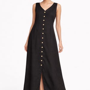 Könnte beinhalten: Schwarzes ärmelloses Kleid mit V-Ausschnitt und Knopfleiste. Das lange Kleid hat einen Schlitz vorne und wird mit beigen Absätzen getragen. Die Knöpfe sind goldfarben. Die Kleidlänge beträgt ca. 130 cm.
