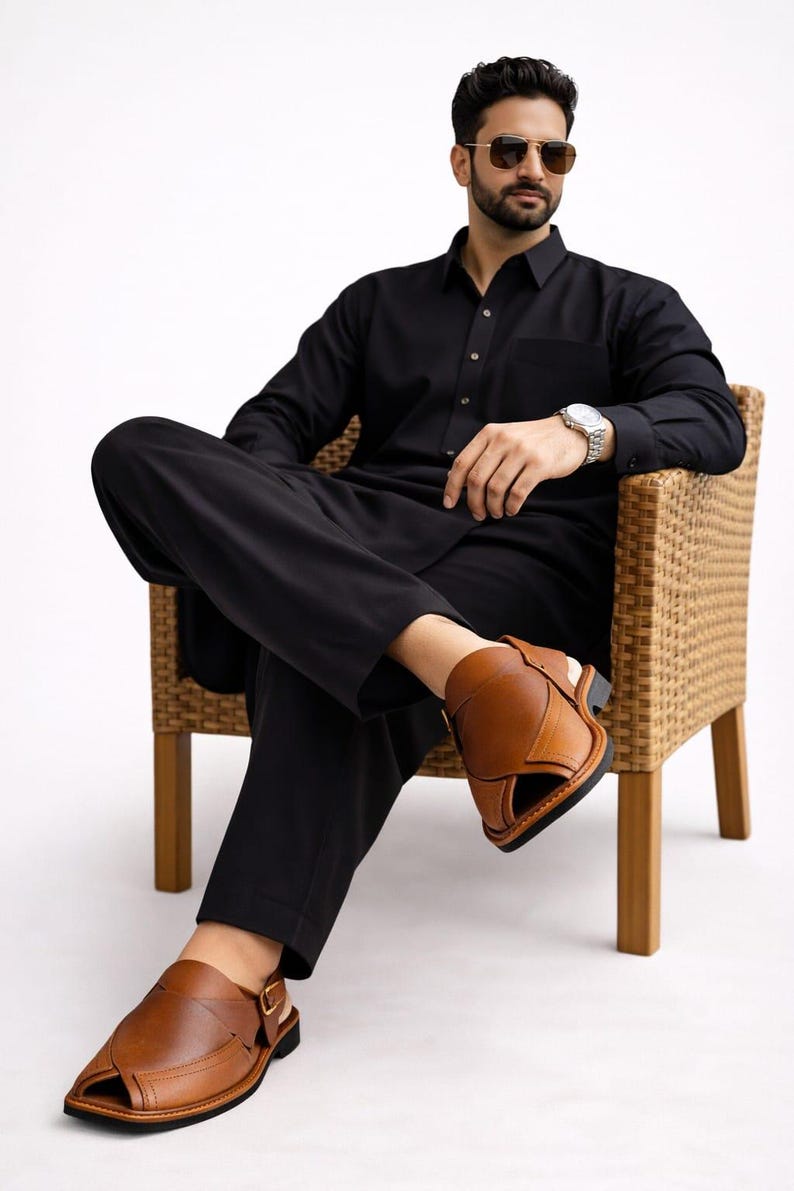 May include: A person wearing a black outfit, including a long-sleeved shirt and pants, is seated in a wicker chair. The person is wearing brown leather sandals. The outfit is suitable for formal or casual wear.