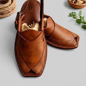 May include: A pair of brown leather Peshawari sandals. The sandals have a unique design with a strap that goes over the top of the foot and a loop for the big toe. The sandals are made of high-quality leather and are perfect for everyday wear.