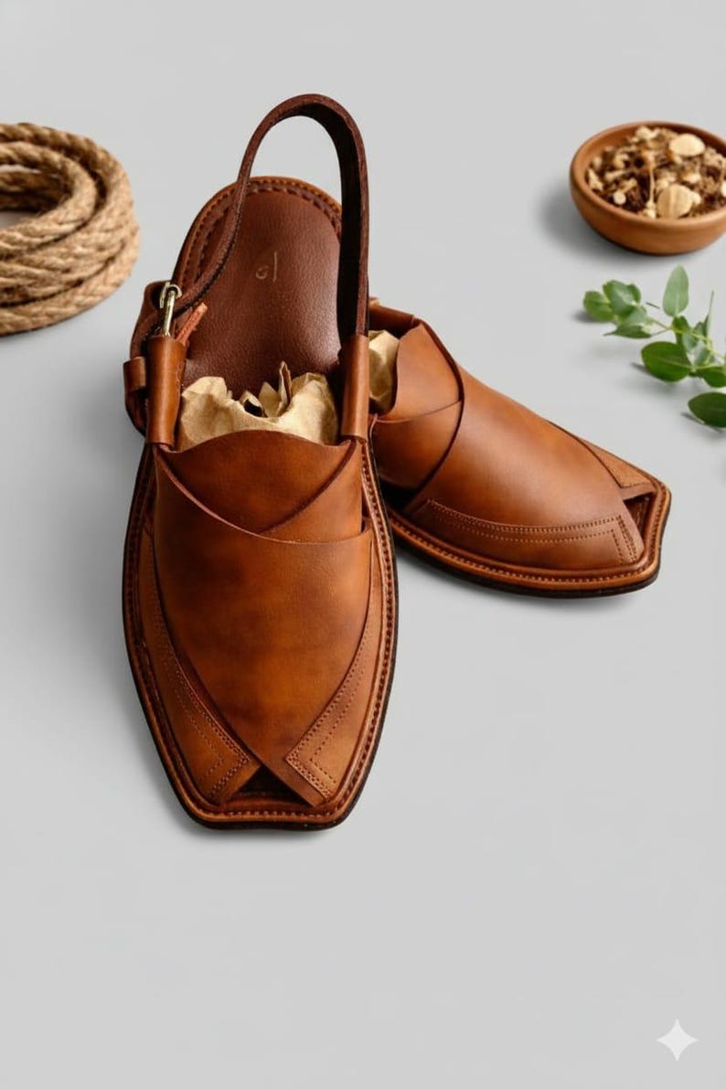 May include: A pair of brown leather Peshawari sandals. The sandals have a unique design with a strap that goes over the top of the foot and a loop for the big toe. The sandals are made of high-quality leather and are perfect for everyday wear.